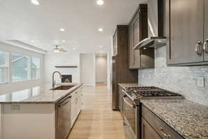 Kitchen featuring stainless steel appliances, light stone countertops, wall chimney exhaust hood, a warm lit fireplace, and recessed lighting