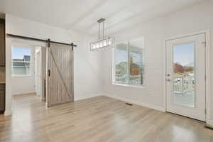 Unfurnished dining area with a barn door, light wood finished floors, and a chandelier