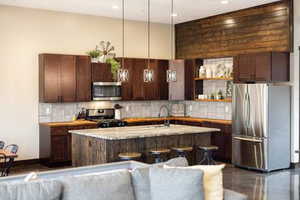 Kitchen with decorative light fixtures, a center island with sink, dark brown cabinetry, stainless steel appliances, and open floor plan