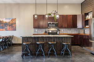 Kitchen featuring a center island with sink, dark brown cabinetry, tasteful backsplash, pendant lighting, and appliances with stainless steel finishes