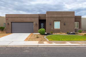 Adobe home with stucco siding, driveway, an attached garage, and a front yard