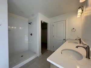 Full bath featuring a spacious closet, double vanity, a textured ceiling, light tile patterned flooring, and walk in shower