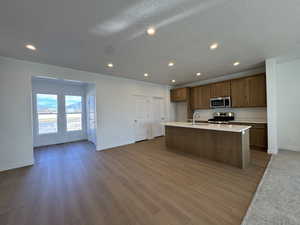 Kitchen featuring recessed lighting, a center island with sink, a textured ceiling, appliances with stainless steel finishes, and brown cabinetry