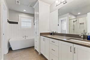 Bathroom featuring double vanity, a shower stall, a freestanding tub, light tile patterned flooring, and a textured ceiling