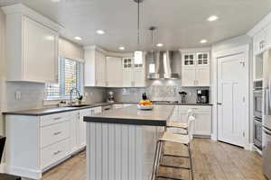 Kitchen featuring a kitchen island, dark countertops, wall chimney exhaust hood, pendant lighting, and a kitchen bar