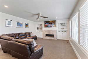 Living area featuring built in shelves, a tiled fireplace, carpet floors, ceiling fan, and recessed lighting