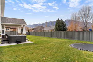 Fenced backyard featuring a mountain view, a patio area, a trampoline, and a hot tub