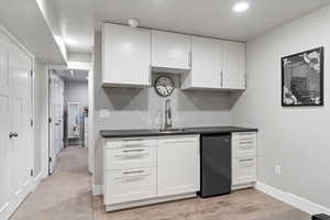 Kitchen featuring dark countertops, black fridge, white cabinets, recessed lighting, and light wood-style floors