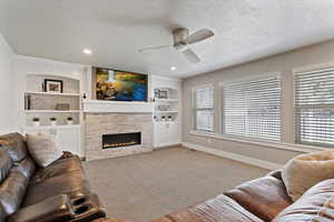 Living area featuring a textured ceiling, light carpet, a ceiling fan, a tiled fireplace, and built in shelves