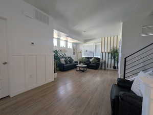 Living area with a decorative wall, stairway, wood finished floors, and a wainscoted wall