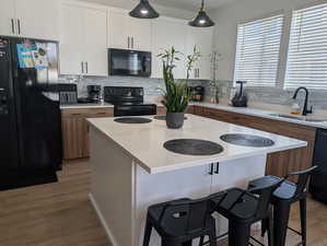 Kitchen with white cabinetry, black appliances, decorative backsplash, pendant lighting, and light wood-type flooring