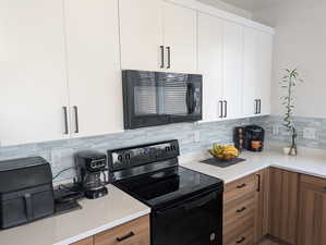 Kitchen with black appliances, modern cabinets, white cabinets, brown cabinets, and tasteful backsplash