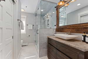Full bathroom featuring vanity, light tile patterned flooring, a stall shower, and a baseboard heating unit