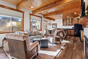 Living room featuring plenty of natural light, dark wood-type flooring, a wooden ceiling with exposed beams, a lit fireplace, and recessed lighting