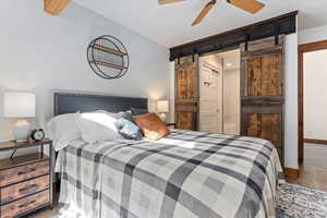 Bedroom with wood finished floors, a barn door, connected bathroom, and ceiling fan