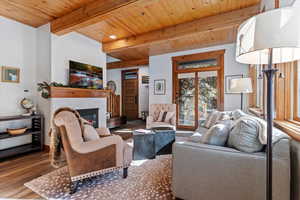 Living area featuring wood finished floors, a glass covered fireplace, and a wood ceiling with exposed beams