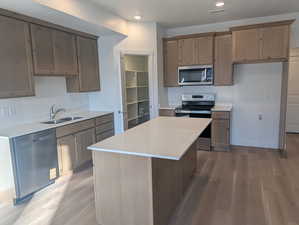 Kitchen with stainless steel appliances, light wood-type flooring, a kitchen island, recessed lighting, and light stone counters