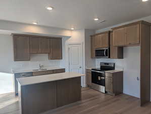 Kitchen featuring stainless steel appliances, dark wood finished floors, a center island, recessed lighting, and a textured ceiling
