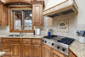 Kitchen with light stone counters, custom range hood, stainless steel gas cooktop, and brown cabinets