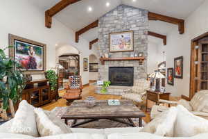 Living room featuring wood finished floors, a fireplace, arched walkways, beamed ceiling, and high vaulted ceiling