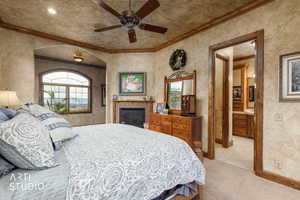 Bedroom with crown molding, ensuite bath, ceiling fan, light colored carpet, and a brick fireplace