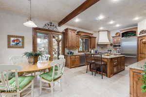 Kitchen with hanging light fixtures, stainless steel appliances, light stone countertops, a center island with sink, and decorative backsplash