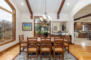 Dining room featuring beamed ceiling, light wood-type flooring, a chandelier, and arched walkways