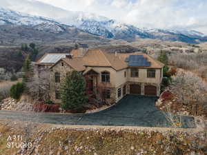 View of front of home featuring stone siding, a mountain view, driveway, solar panels, and stucco siding