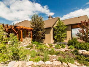 Pueblo-style home featuring a pergola, stucco siding, a shingled roof, a chimney, and a patio area