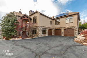 View of front of property featuring stone siding, roof mounted solar panels, a chimney, and stucco siding