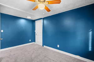 Carpeted empty room featuring a textured ceiling and ceiling fan