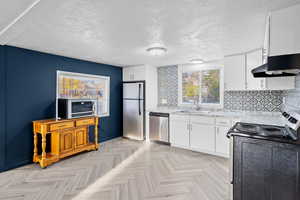 Kitchen featuring appliances with stainless steel finishes, white cabinets, a textured ceiling, tasteful backsplash, and under cabinet range hood