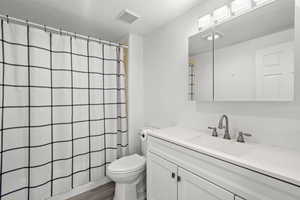 Full bathroom with a textured ceiling, curtained shower, vanity, and dark wood-style floors