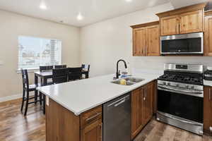 Kitchen featuring appliances with stainless steel finishes, dark wood-style floors, a peninsula, recessed lighting, and brown cabinetry