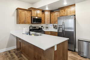 Kitchen featuring appliances with stainless steel finishes, brown cabinetry, a peninsula, dark wood-type flooring, and recessed lighting