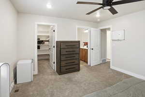 Bedroom with light carpet, a walk in closet, recessed lighting, a ceiling fan, and ensuite bath