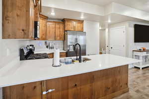 Kitchen with brown cabinetry, a peninsula, appliances with stainless steel finishes, light stone countertops, and light wood-type flooring