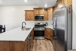 Kitchen with stainless steel appliances, a peninsula, light wood-style flooring, brown cabinets, and recessed lighting