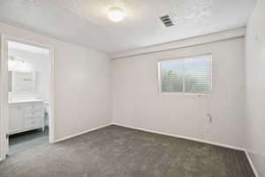 Unfurnished bedroom featuring dark colored carpet, a textured ceiling, and ensuite bath