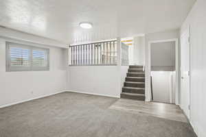 Empty room featuring carpet floors, a textured ceiling, and stairs