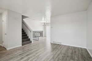 Unfurnished living room featuring light wood-style floors, a chandelier, and stairs