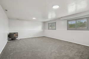 Unfurnished living room featuring a wood stove, carpet floors, healthy amount of natural light, and a textured ceiling