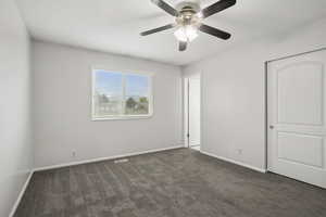 Unfurnished bedroom with dark colored carpet, ceiling fan, and a closet