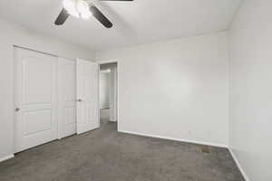 Unfurnished bedroom with dark colored carpet, a closet, and a ceiling fan