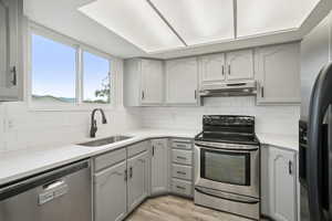 Kitchen featuring gray cabinets, appliances with stainless steel finishes, light stone counters, under cabinet range hood, and light wood finished floors