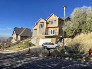 View of front facade featuring a balcony, stucco siding, a garage, and driveway