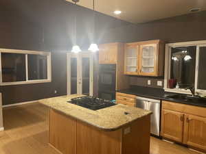 Kitchen featuring decorative light fixtures, a center island, light wood-style floors, black appliances, and dark stone countertops