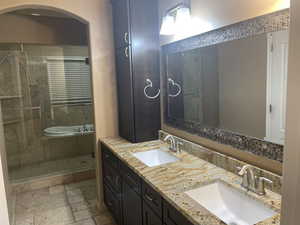 Bathroom with double vanity, stone tile flooring, and a shower stall