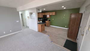 Kitchen featuring wood finish cabinetry, dark countertops, black appliances, recessed lighting, and light colored carpet