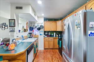 Kitchen featuring stainless steel refrigerator with ice dispenser, light wood finished floors, a textured ceiling, black range oven, and dishwasher